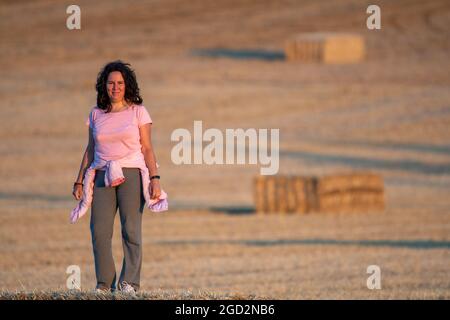 donna latina e brunetta di mezza età che indossa abbigliamento sportivo rosa e grigio camminando in campagna in un ambiente rurale. Messa a fuoco selettiva. Guardando è venuto Foto Stock