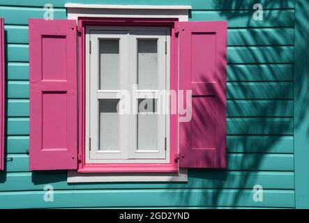 Vibrante edificio e finestra color turchese caraibico con persiane rosa Foto Stock