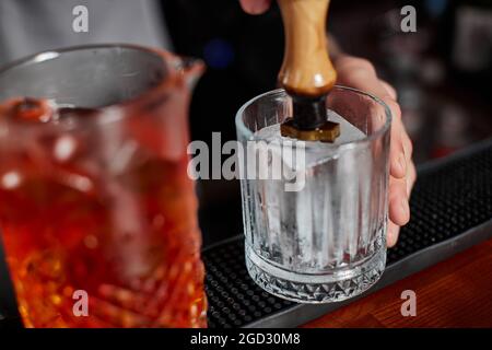 il barman in grembiule versa un cocktail vecchio stile in un bicchiere Foto Stock