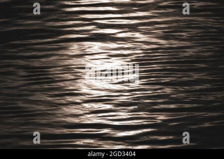 Acqua splendente con riflessi. Motivo metallico della superficie dell'acqua ondulata. Primo piano della texture delle onde Foto Stock