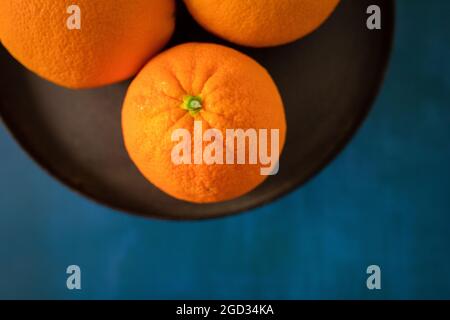 Una ciotola o un piatto di arance ombelico vibranti su uno sfondo blu intenso Foto Stock