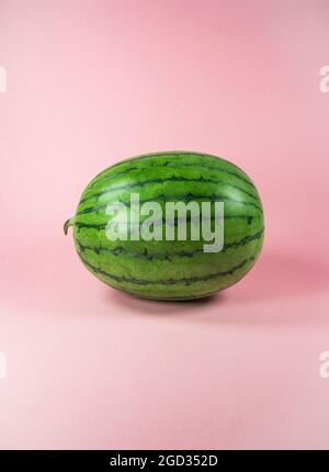Cocomero fresco su sfondo rosa pastello alla moda. Frutta tropicale minima e concetto estivo. Foto Stock