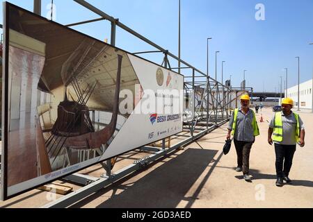 Giza, Egitto. 10 agosto 2021. I lavoratori camminano oltre un manifesto sulla barca solare del re Khufu al Grand Egyptian Museum di Giza, Egitto, il 10 agosto 2021. I funzionari egiziani hanno evidenziato martedì il recente successo del trasporto di un'enorme e fragile barca faraonica di 4,600 anni da un vecchio museo al nuovo Grand Egyptian Museum (GEM) a circa 10 km di distanza. La barca solare lunga 42 metri e lunga 20 tonnellate è stata scoperta nel 1954 accanto alla Grande Piramide di Giza che apparteneva al re Khufu. Credit: Ahmed Gomaa/Xinhua/Alamy Live News Foto Stock