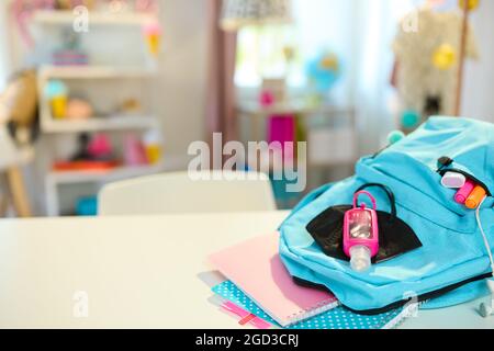 Ritorno a scuola. Closeup su tavolo bianco con libri da lavoro, stazionario, zaino, maschera ffp2 e antisettico in camera degli studenti in giornata di sole. Foto Stock