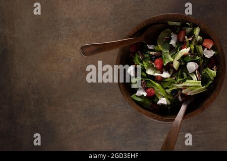 Un rustico fondo marrone testurizzato con forchetta di legno scuro e cucchiaio servendo utensili e una sana insalata Foto Stock