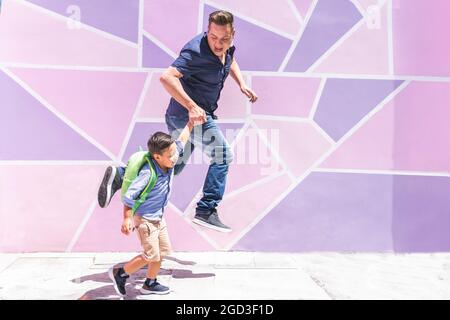 Padre e figlio saltano e corrono a scuola su uno sfondo urbano viola e rosa. Ritorno a scuola Foto Stock