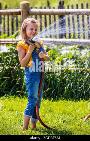 Giovane ragazza spruzzando acqua con tubo da giardino in cortile erboso Foto Stock