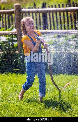 Giovane ragazza spruzzando acqua con tubo da giardino in cortile erboso Foto Stock