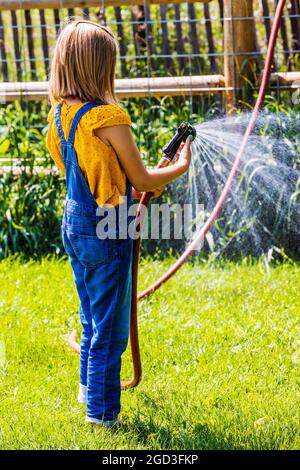 Giovane ragazza spruzzando acqua con tubo da giardino in cortile erboso Foto Stock