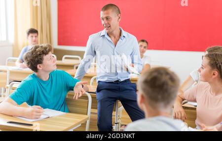 Insegnante positivo che aiuta gli studenti adolescenti durante la lezione Foto Stock