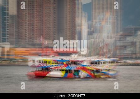 Trattamento di sfocatura zoom della 'Night Star', una delle flotte Star Ferry, passando per gli alti blocchi di appartamenti di Union Square, West Kowloon Foto Stock