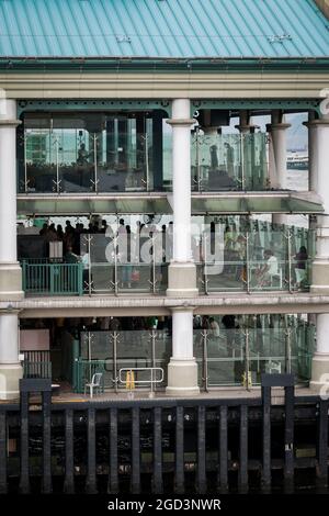 I turisti e la gente del posto aspettano di salire a bordo di uno Star Ferry al Molo 7 del Central Ferry sull'Isola di Hong Kong per attraversare il Victoria Harbour fino a Tsim Sha Tsui a Kowloon Foto Stock