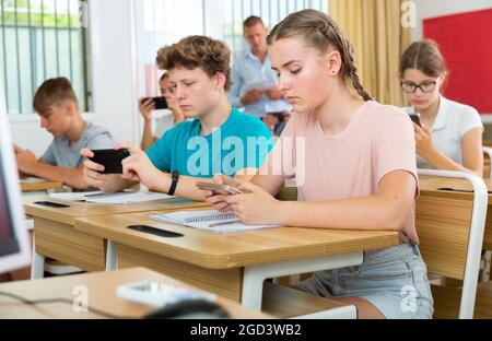 Gruppo di adolescenti moderni seduti con telefoni cellulari in lezione Foto Stock