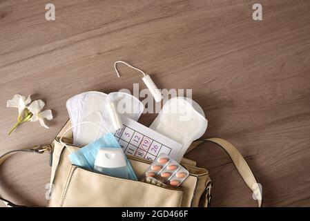 Borsetta con vari prodotti per l'igiene mestruale e protezione covid-19 per le donne su tavolo di legno. Vista dall'alto. Foto Stock