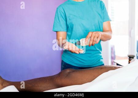 Operaio termale femminile senza volto che dà massaggio del corpo al cliente africano e che usa l'olio. Foto Stock