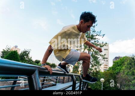 Ragazzo fresco e sicuro che pratica trucchi parkour in città e divertirsi. Foto Stock