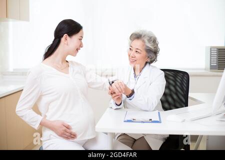Medico tenendo la donna incinta della pressione del sangue Foto Stock