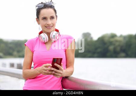 La giovane donna sorridente con le cuffie sul collo tiene lo smartphone nelle mani Foto Stock