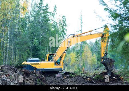 L'escavatore esegue il lavoro di un bulldozer con un parasassi di pala nella disboscatura e nella spianatura del terreno per cantieri edili Foto Stock