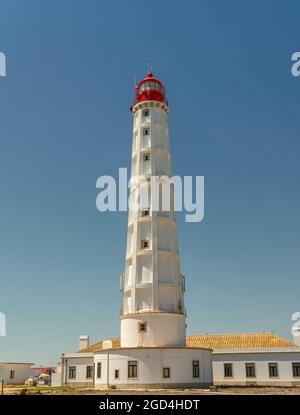 Un faro bianco con una cima rossa, contro il cielo blu. Su una spiaggia di sabbia. Spazio di copia Foto Stock