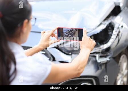 L'agente donna scatta foto dei danni all'auto dopo un incidente dallo smartphone. Conseguenze del concetto di incidente automobilistico Foto Stock