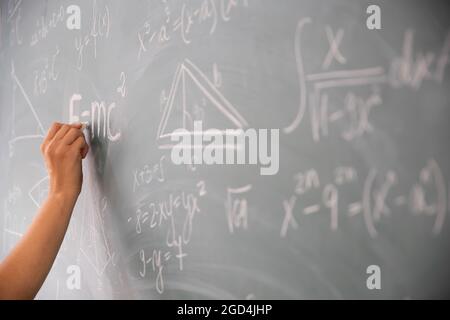 Primo piano di una mano che tiene gesso e scrive equazioni matematiche sulla lavagna. Concetto di istruzione. Foto Stock