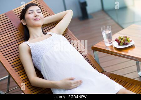 Donna incinta che prende un pisolino sulla chaise longue Foto Stock
