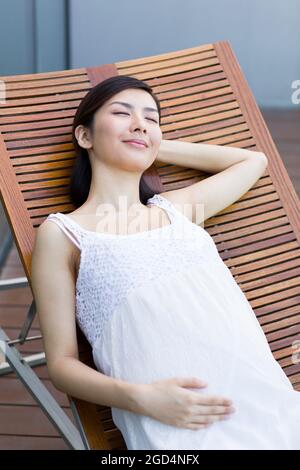 Donna incinta che prende un pisolino sulla chaise longue Foto Stock