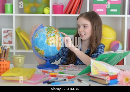 Ragazza che si siede a tavola con il globo e studia Foto Stock