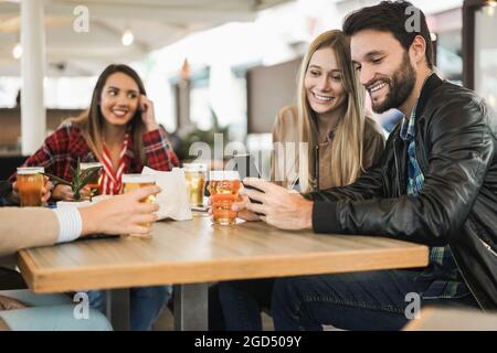 I giovani si divertono con il telefono cellulare mentre bevono birra al bar ristorante - Focus sul volto dell'uomo Foto Stock