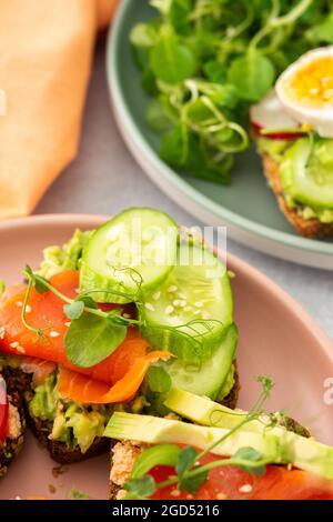 Sana e gustosa colazione, panini con avocado e salmone, cetrioli e pomodori, ravanelli e micrograni di piselli con uova sode e insalata di radice Foto Stock