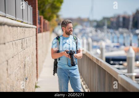 Uomo tenere la macchina fotografica in piedi sulla passeggiata. Fotografia di vacanza. Fotografia di viaggio Foto Stock