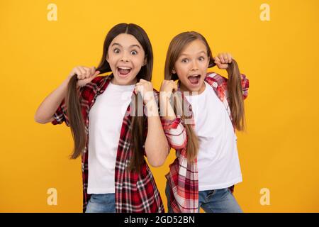 i bambini stupiti nella camicia casual a scacchi tengono lunghi capelli lisci su sfondo giallo, acconciatura Foto Stock