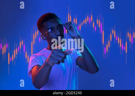Giovane uomo africano che punta su sfondo viola con grafico commerciale in concetto grafico. Foto Stock