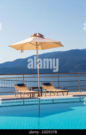 Piscina di lusso con sedie a sdraio vuote e ombrellone presso il resort con splendida vista mare. Foto Stock