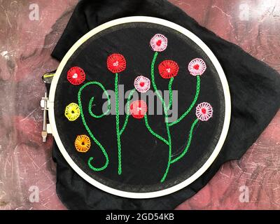 Cuciture a maglia e fiori ricamati a mano con linee a stelo a maglia a catena sul tessuto in poplin nero in ricamo tessile Foto Stock