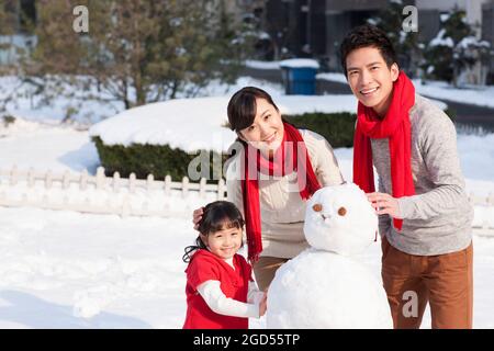 Felice famiglia costruendo pupazzo di neve Foto Stock