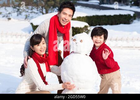 Felice famiglia costruendo pupazzo di neve Foto Stock