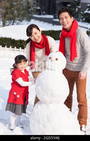 Felice famiglia costruendo pupazzo di neve Foto Stock