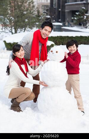 Felice famiglia costruendo pupazzo di neve Foto Stock