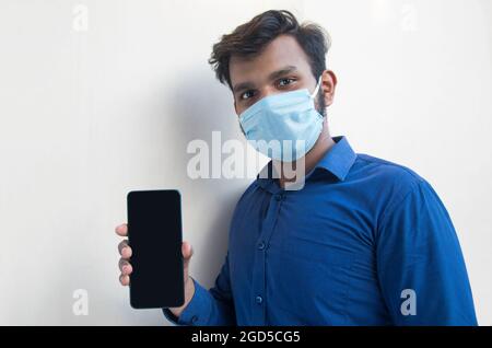 Un giovane con maschera facciale e telefono cellulare Foto Stock