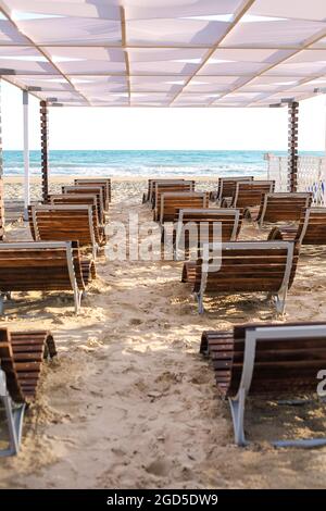 Splendida vista sul mare estivo e sulla spiaggia di sabbia, solitari e vuoti comodi lettini sotto l'ombrellone in piedi sulla riva, sera in hotel resort Foto Stock