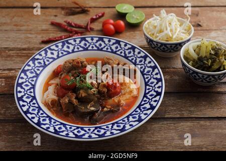 Cibo locale tailandese settentrionale noodle di riso con maiale in piccante zuppa su sfondo di legno Foto Stock