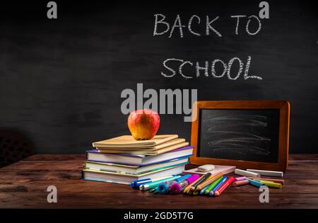 Mucchio di libri e libri di esercizi con shool si applica e spuntino di mela con lavagna. Concetto di ritorno a scuola. Foto Stock