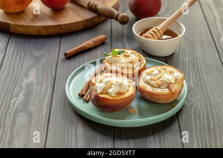 Pesche mature al forno con cannella, petali di mandorle, formaggio cremoso e miele sul tavolo di legno. Messa a fuoco selettiva Foto Stock