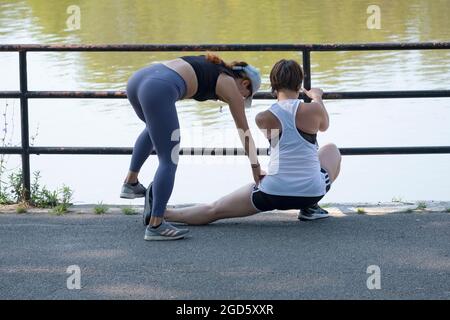 Un addestratore personale molto in forma prende un cliente con gli esercizi di stretching del groin in un parco a Flushing, Queens, New York City. Foto Stock