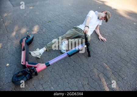 Un giovane è entrato in un incidente su uno scooter elettronico, si trova sull'asfalto e grida di dolore. Foto Stock