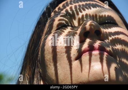 Closeup colpo di foglia di felce ombra su una ragazza asiatica faccia, primo piano di una ragazza reale faccia con pori Foto Stock