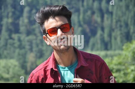 Primo piano di un giovane ragazzo dell'India del Nord in posa all'aperto con una camicia rossa e occhiali da sole rossi da guardare con la macchina fotografica Foto Stock