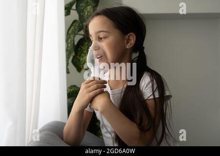 La bambina fa l'inalazione con un nebulizzatore. Bambino malato che tiene l'inalatore in mano e respira attraverso un inalatore a casa Foto Stock